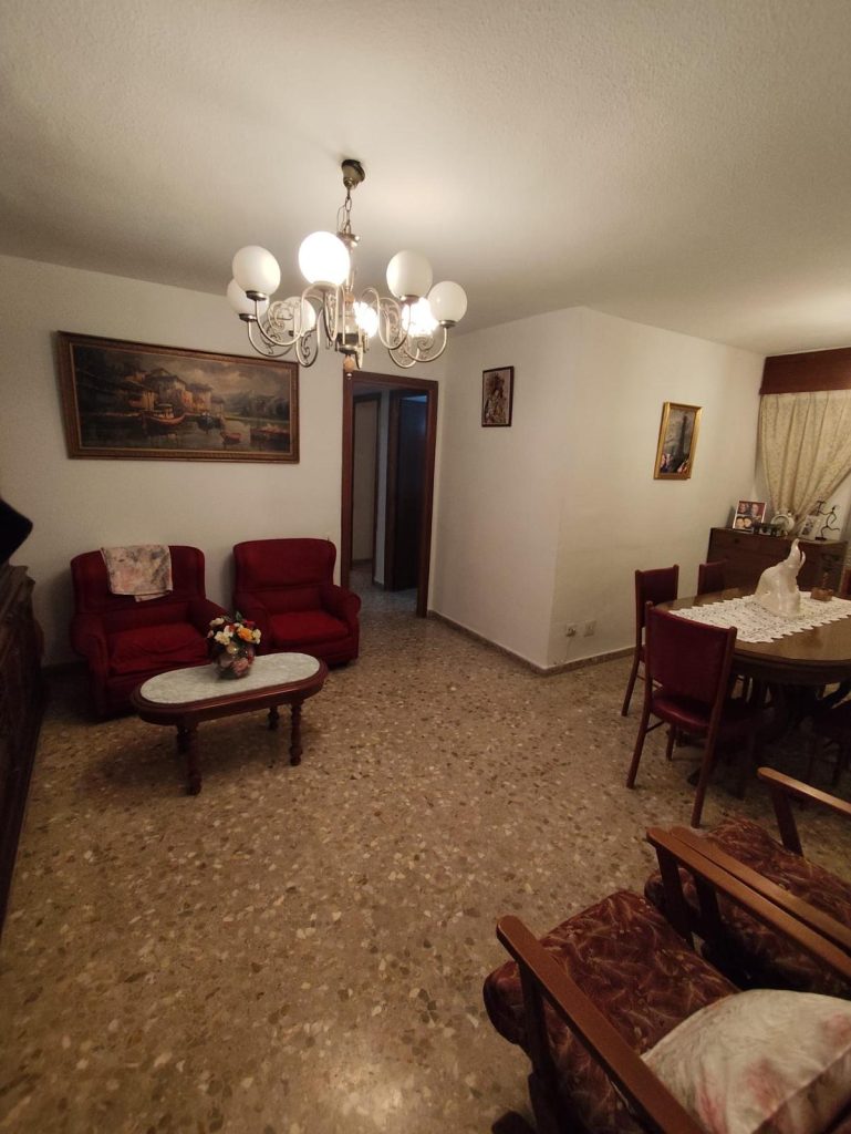 Sala de estar con sofás rojos, mesa de centro, comedor, cuadros y candelabro en el techo.